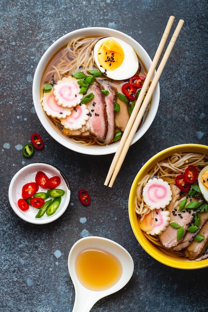 Cooking Japanese noodle soup ramen. Ramen with sliced pork, narutomaki, egg and kitchen spoon with broth on rustic stone background. Making traditional dish of Japan, top view, close-up, concept