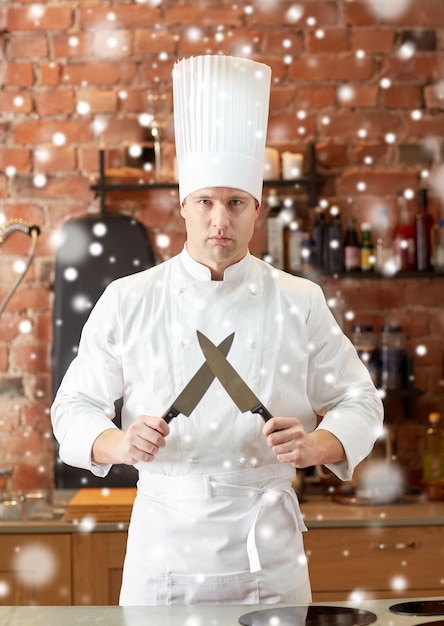 Concetto di cucina, utensili da cucina e persone - cuoco maschio felice con coltello nella cucina del ristorante sopra l'effetto neve