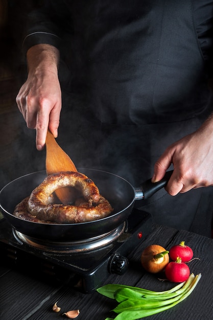 레스토랑 주방에서 고기 소시지 요리. 요리사 또는 프라이팬에 감자 튀김 소시지를 요리하십시오. 맛있는 고기 다이어트의 아이디어