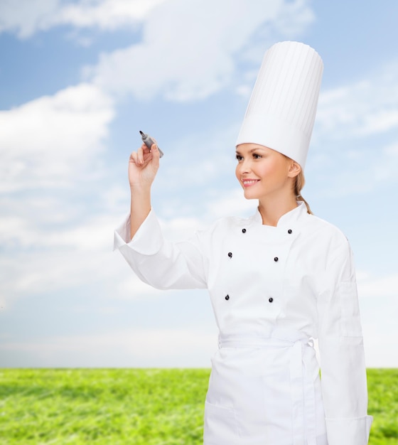 cooking, new technology , advertisement and food concept - smiling female chef with marker writing something on virtual screen