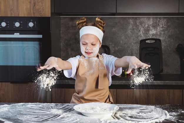 写真 子供のためのクッキングまたは料理学校子供手と顔に小麦粉を塗った小さな女の子がモーション ショットでテーブルに小麦粉を投げます