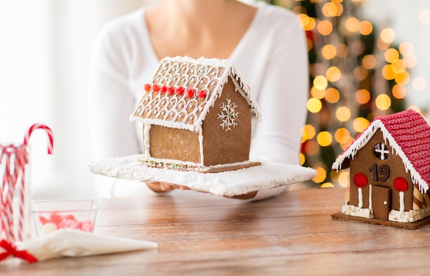 cooking, people, christmas and baking concept - close up of happy woman holding and showing gingerbread house at home