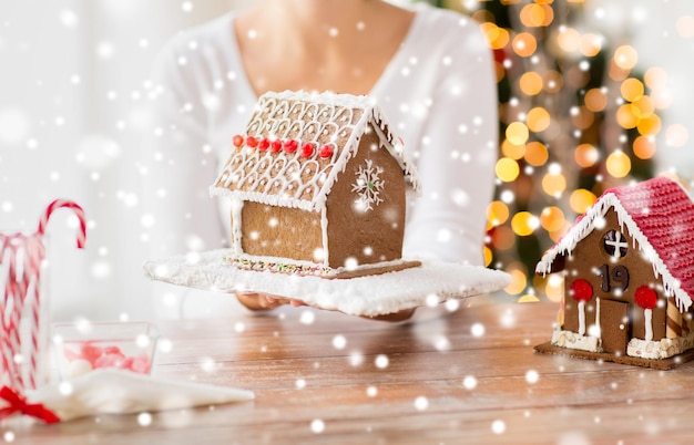 cooking, people, christmas and baking concept - close up of happy woman holding and showing gingerbread house at home