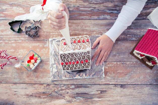 cooking, people, christmas and decoration concept - close up of happy woman making gingerbread houses at home