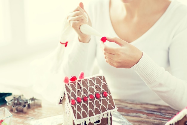 cooking, people, christmas and decoration concept - close up of happy woman making gingerbread houses at home