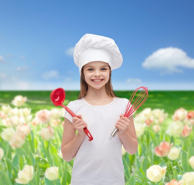 cooking and people concept - smiling little girl in cook hat with ladle and whisk