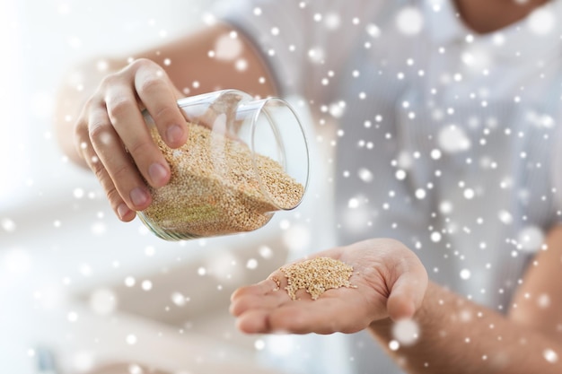 cooking, people and home concept - close up of male emptying jar with quinoa