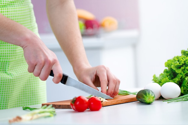 Cucina persona in grembiule tritare prodotti eco-compatibili per insalata di verdure fresche sane in cucina a casa.