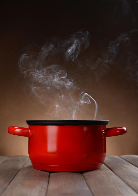 Cooking pot with steam on table on brown background