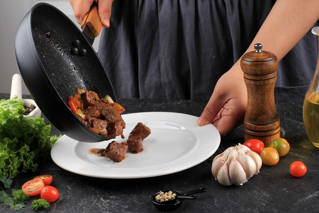 Processo di cottura, chef donna asiatica mettere alla griglia wagyu fatty saikoro dadi a cubetti bistecca di manzo con salsa barbecue sulla padella nera alla piastra bianca