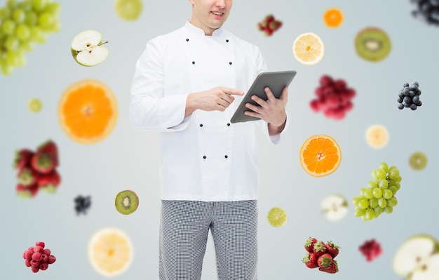 料理、職業、人々 のコンセプト - 灰色の背景に果物や果実の上にタブレット pc コンピューターを保持している幸せな男性シェフのクローズ アップ