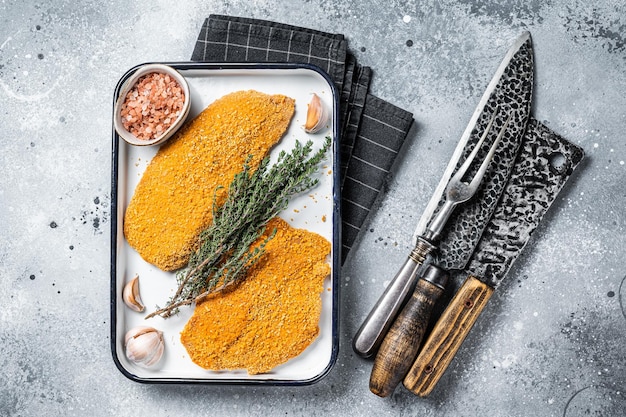 Cooking raw chicken schnitzel in breadcrumbs uncooked meat steak Gray background Top view