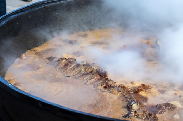 Cucinare il vero pilaf uzbeko stufare le costolette di agnello in un enorme calderone con tanto vapore all'esterno durante una tradizionale festa popolare