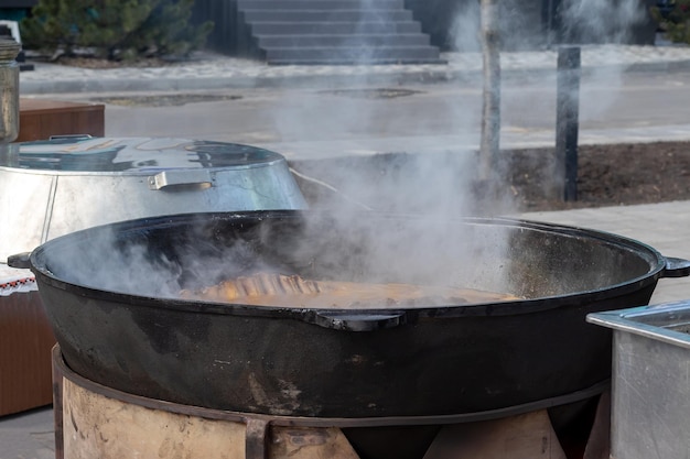Cooking real Uzbek pilaf Stewing lamb ribs in a huge cauldron with lots of steam outside during a traditional folk festival
