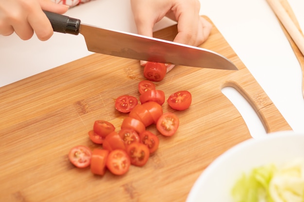 Cooking Salad. Female hands cut cherry tomatoes for Caesar.