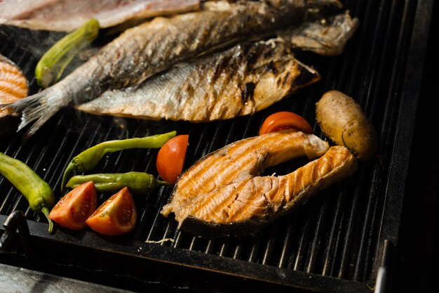 Cooking seafood mix of salmon sea bass and vegetables Grilling fish with chili potatoes and tomato