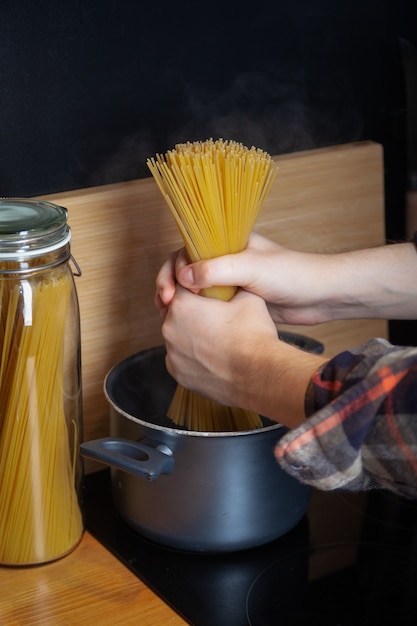 cooking spaghetti in pot with boiling water, male hands put pasta in pan