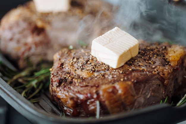 贅沢なステーキをグリル鍋で調理し、バターをステーキの上に広げ、挽いたコショウと塩をローズマリーの小枝で味付けします