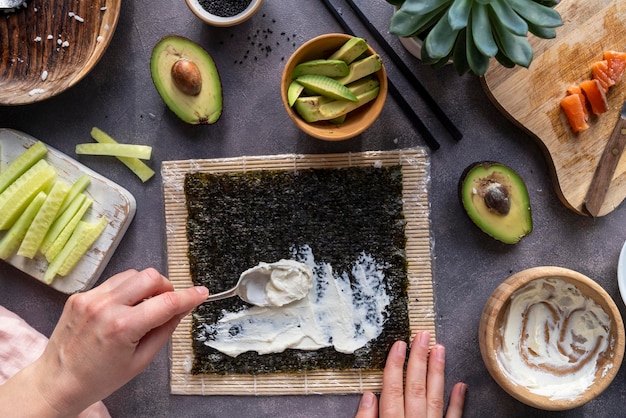 Cucinare involtini di sushi a casa con salmone, avocado e cetriolo mano femminile che prepara il sushi di avocado passo dopo passo