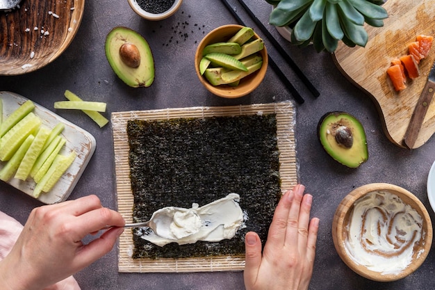 Cooking Sushi rolls at home with salmon avocado and cucumber Female hand preparing avocado sushi top view Step by step