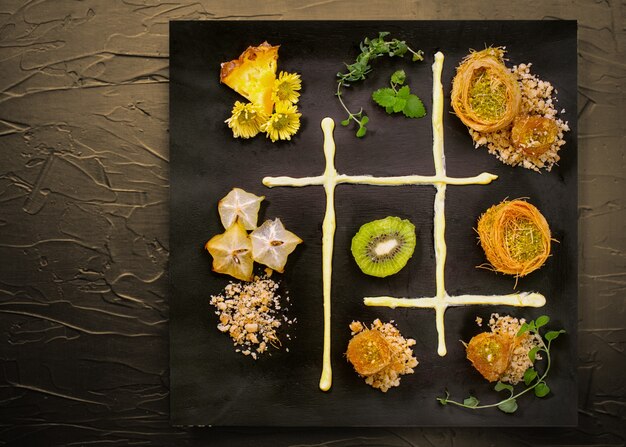 Cooking sweets turkish traditional ramadan pastry dessert kunafa (kadaif, baklava),kiwi,ananas,nuts ,dark  background.Plate art composition.