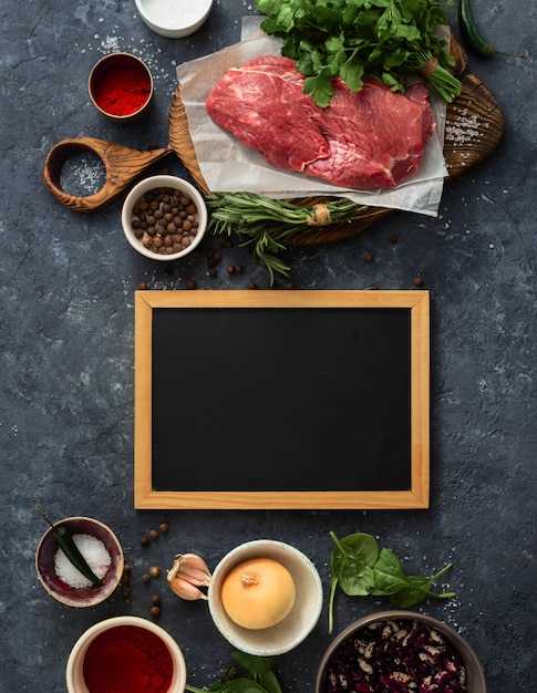 Cooking table with blank chalkboard and beef meat, vegetables and spices