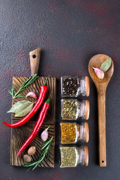 Cooking table with spices in glass jars  and herbs.  on dark surface