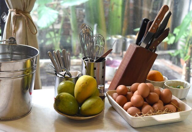 Cooking tools with knifes set and piles of eggs and mango in a kitchen