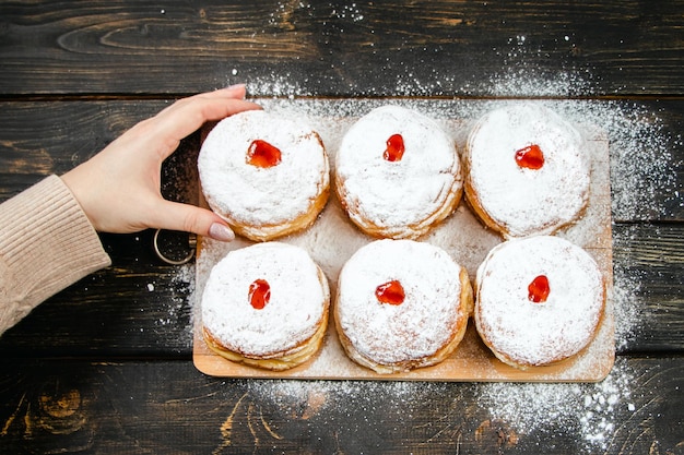 Cooking traditional Hanukkah sufganiyot Woman sprinkles donuts with powdered sugar