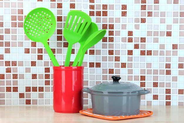 Cooking utensils and pan in kitchen on table on mosaic tiles background