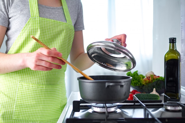 cooking woman in apron standing near stove and cooking soup for dinner