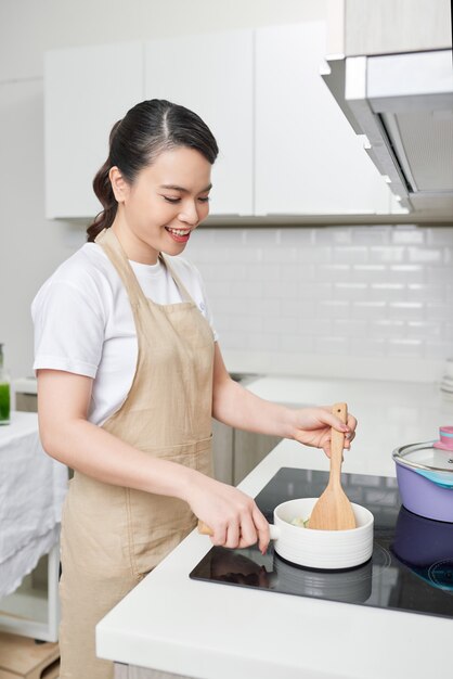 木のスプーンでキッチンで女性を料理