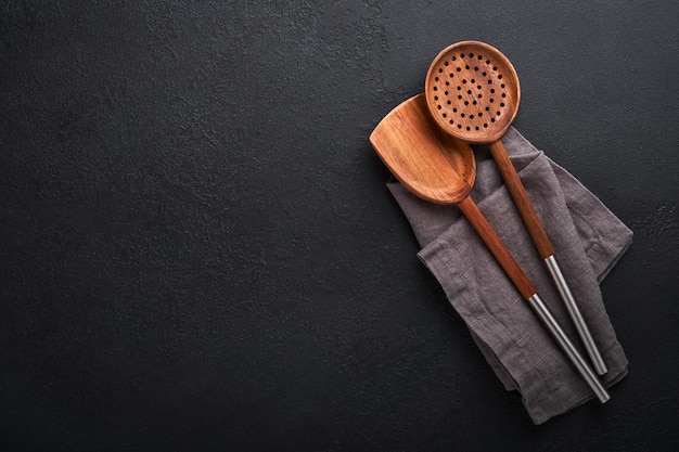 Cooking wooden utensils basil leaves and spices on dark stone background Abstract food background Top view of dark rustic kitchen table with wooden cooking spoon frame Banner for your design