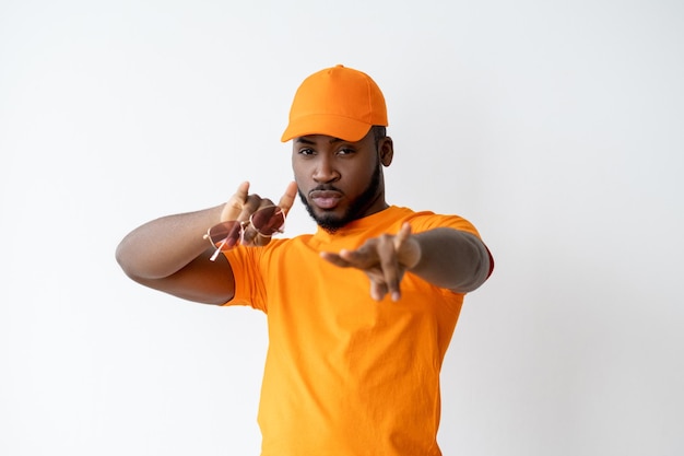 Cool African guy. Urban lifestyle. Summer fashion. Confident stylish dark skin man in bright orange outfit holding sunglasses pointing at camera with hip-hop gesture isolated on white copy space.