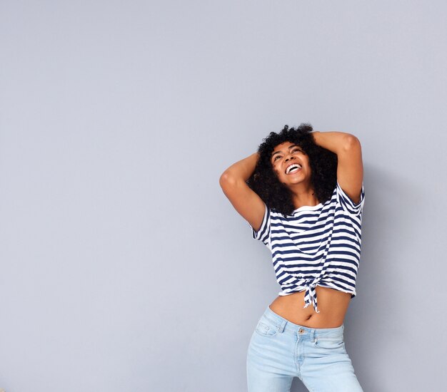 Cool african woman smiling with hands behind head on gray background