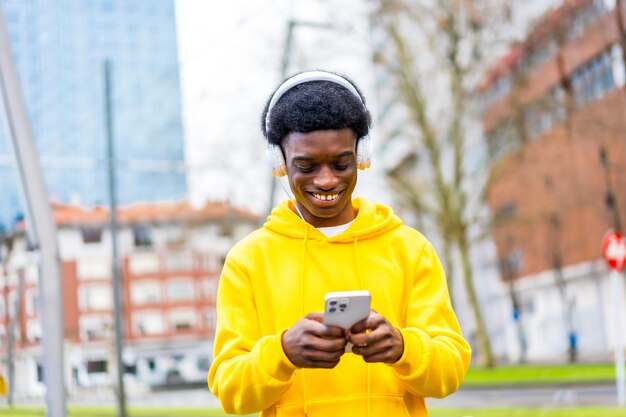 Photo cool african young man listening to music using mobile outdoors