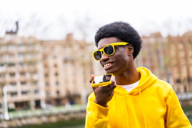 Photo cool african young man sending voice message with mobile outdoors