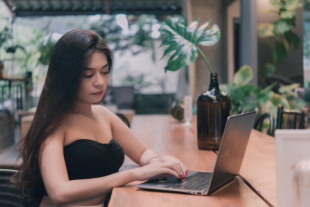 Cool asian girl sitting working with laptop on a wood table in the coffee shopThailand peopleTime for relax