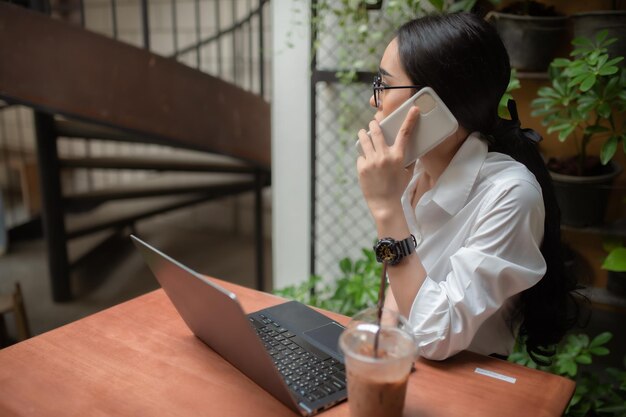 Крутая азиатская девушка сидит и работает с ноутбуком на деревянном столе в кафе