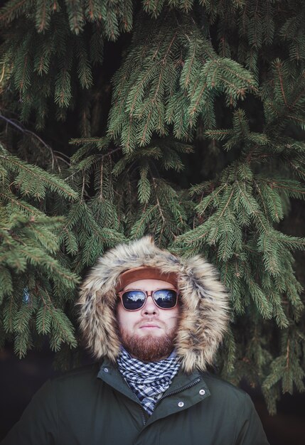 Photo cool bearded man in a winter jacket against a fir tree. space for text