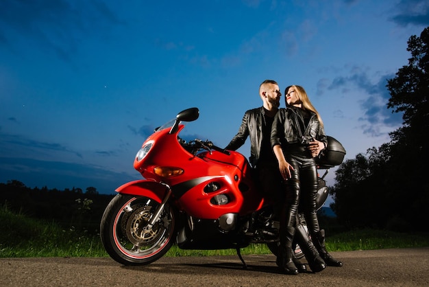 Cool biker couple in leather jackets sitting on red sports bike outdoors