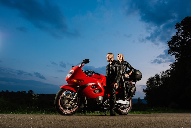 Cool biker couple in leather jackets sitting on red sports bike outdoors