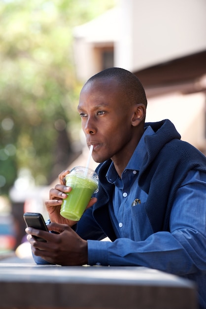 携帯電話と飲み物の外に座っているクールな黒人男