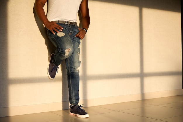 Cool black man in jeans and a white Tshirt stands in the sunlight opposite the window