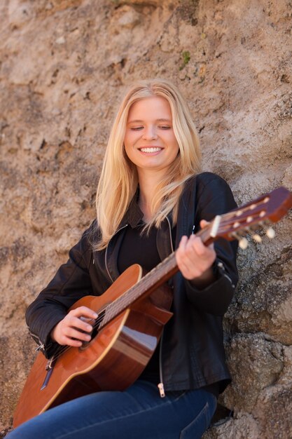 Ragazza bionda fresca che gioca chitarra all'aperto