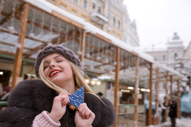 Cool blonde woman holding savory gingerbread against light decoration at the Christmas fair in Kiev