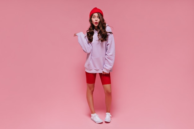 Cool brunette girl in red hat, cycling shorts and purple hoodie whistles