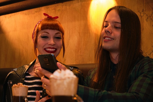 Cool couple looking at the mobile while having a drink. Gossip concept. Travel planning concept