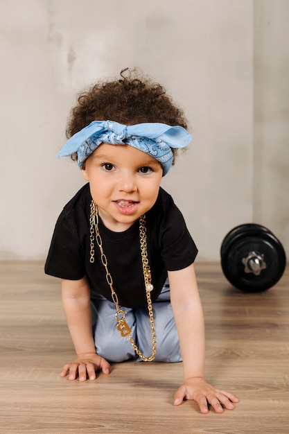 Photo cool cute little girl with afro hair and a blue bandana on the forehead crawling towards camera