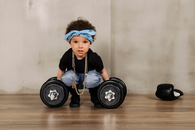 Cool Cute little girl with afro hair and a blue bandana on the forehead pretending to lifting heavy dumbbells